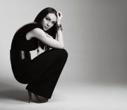 Fashionable young woman wearing black jumpsuit and accessories and sitting in studio.