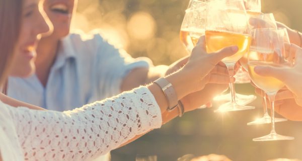 Group of friends having drinks at sunset. They are celebrating with a wine toast. They are smiling and happy. Lens flare