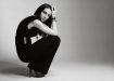 Fashionable young woman wearing black jumpsuit and accessories and sitting in studio.