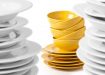 A stack of yellow bowls and plates isolated on white. Selective focus on yellow bowls, blurred white plates.