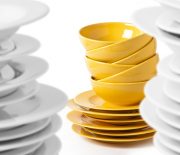 A stack of yellow bowls and plates isolated on white. Selective focus on yellow bowls, blurred white plates.
