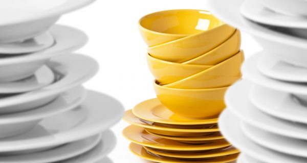 A stack of yellow bowls and plates isolated on white. Selective focus on yellow bowls, blurred white plates.